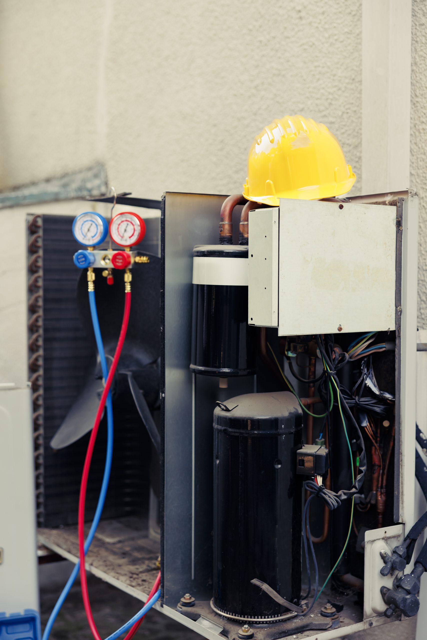 close up of damaged external opened out of service air conditioner unit in need of fixing yellow protection helmet on top of outdoor hvac system with manifold gauges compressors wiring photo